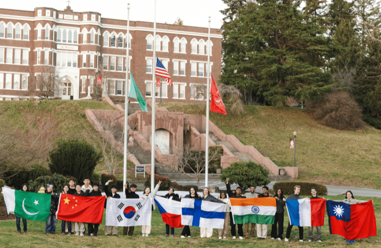 Students hold international flags beneath the flag poles in front of academic building