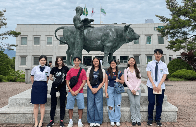 Students stand in front of a statue of a bull and man with a book