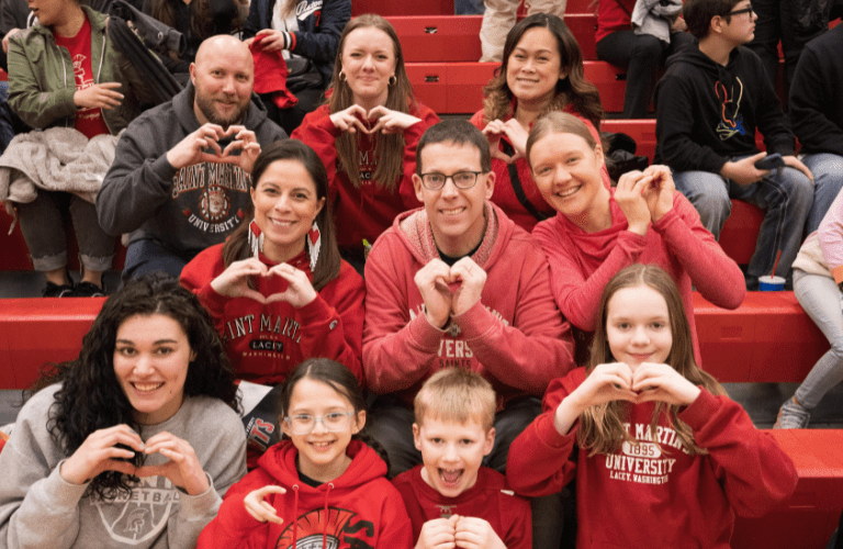 Adults and children in Saint Martin's sweatshirts pose in the stands at a basketball game