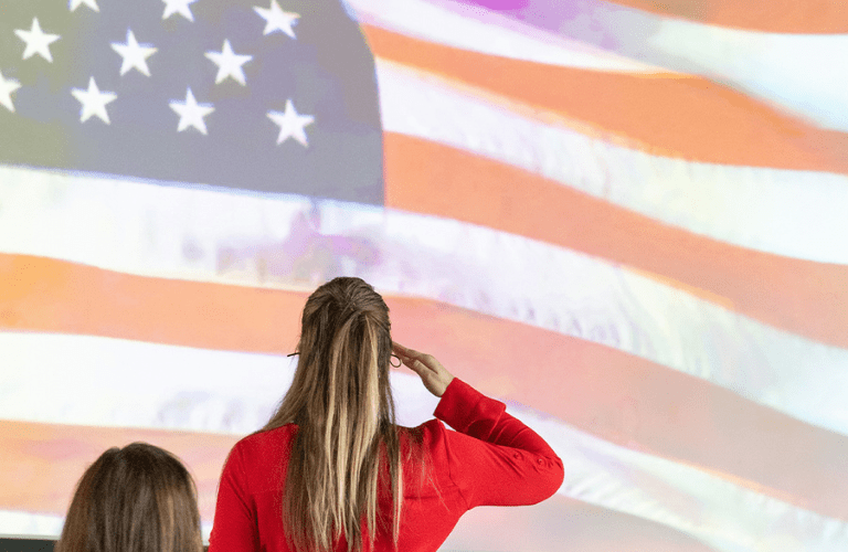 A woman in red stands and salutes the American flag projected on a screen
