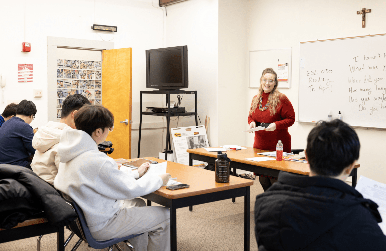 A professor teaches from the front of a class of students