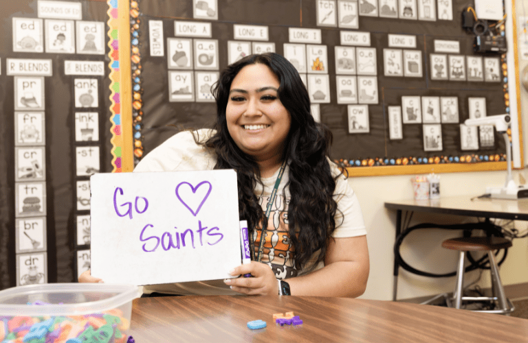A student holds a white board that says "Go Saints" in an elementary classroom