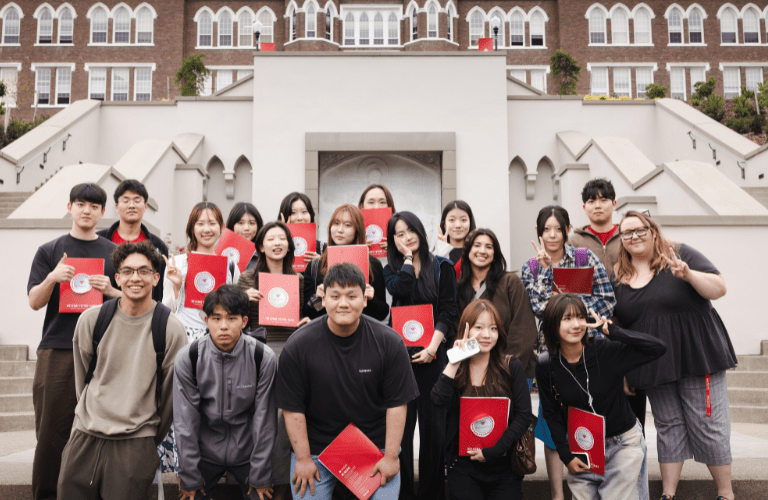 Students hold red folders in front of the grand staircase