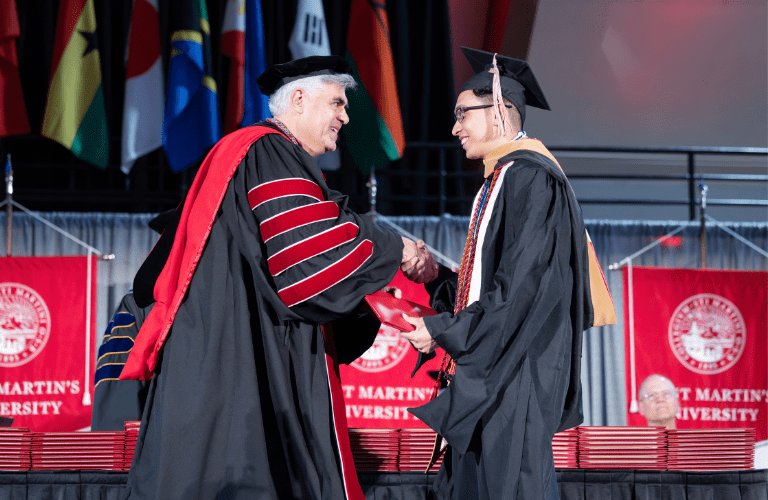 The president shakes hands with a graduate student in robes at commencement