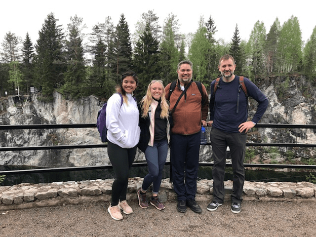 Jamie Olson and students on study abroad trip pose in front of an overlook, with a line of trees in the background