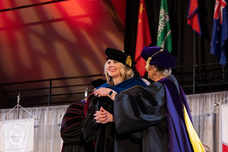 A Ph.D. candidate gets hooded on stage as she receives her doctoral degree