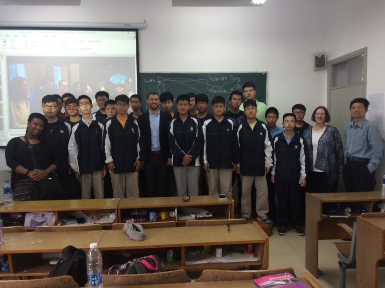 A large group of students and a teacher pose in front of a chalkboard