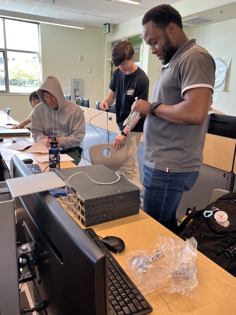 Students work with cables and devices at long rows of desks