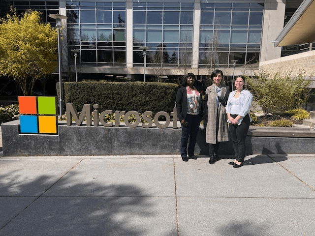 Three women stand in front of the Microsoft logo on Microsoft campus