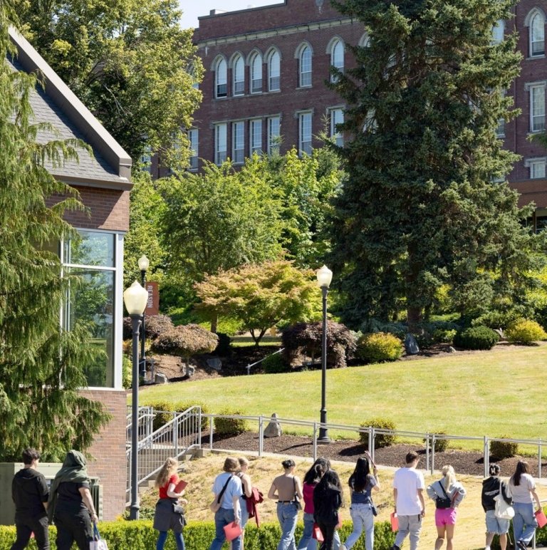 Students walk out in a line from a building, with an old building up the hill