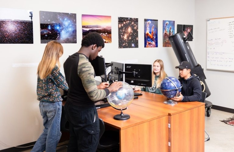 Students work at computers and a globe in classroom with pictures of space