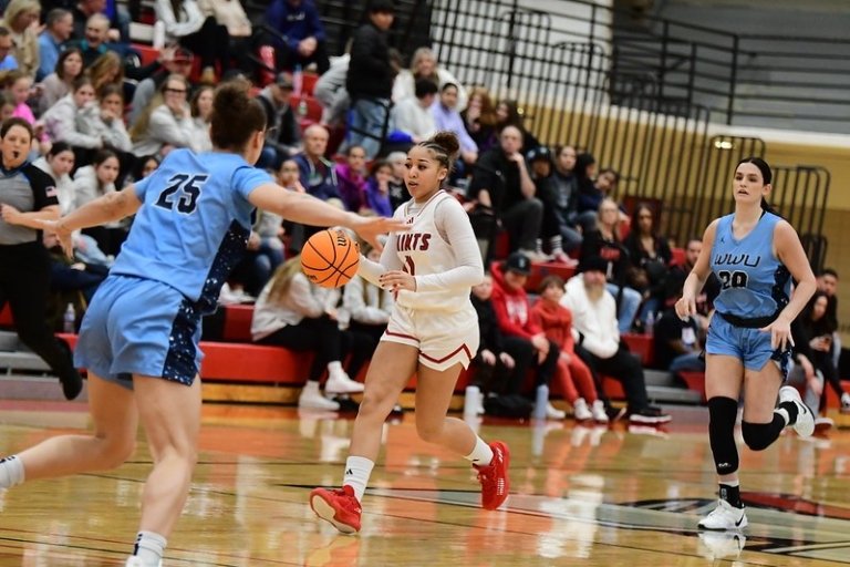 Two teams play basketball with an audience in the stands behind them