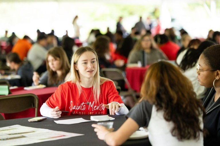 A student in Mentor t-shirt talks with new students at a round table