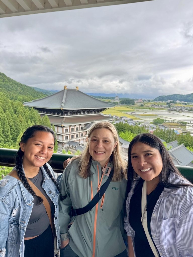 Students and faculty on balcony overlooking rice fields and building with traditional roof