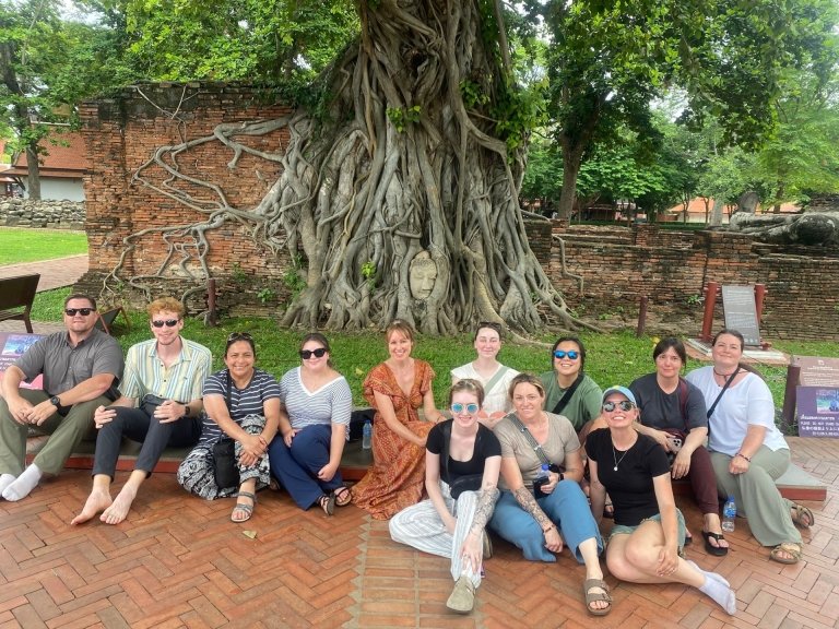 Students and faculty sit beneath a tree with intricate root system