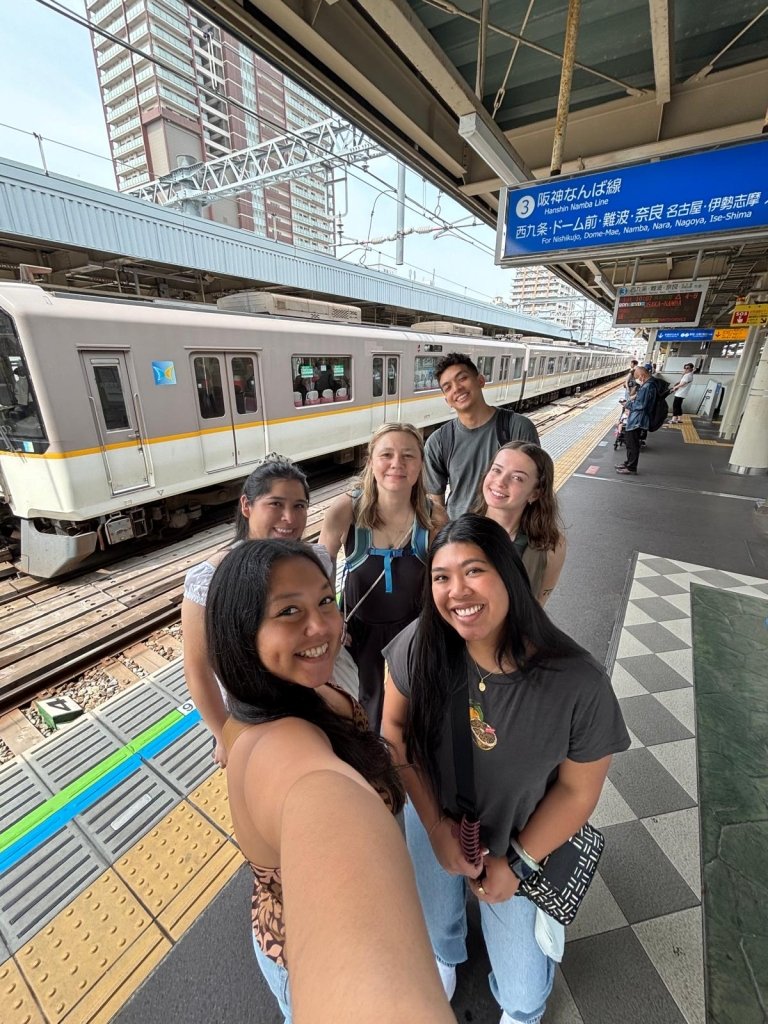 Students pose in front of a train and a sign in Japanese