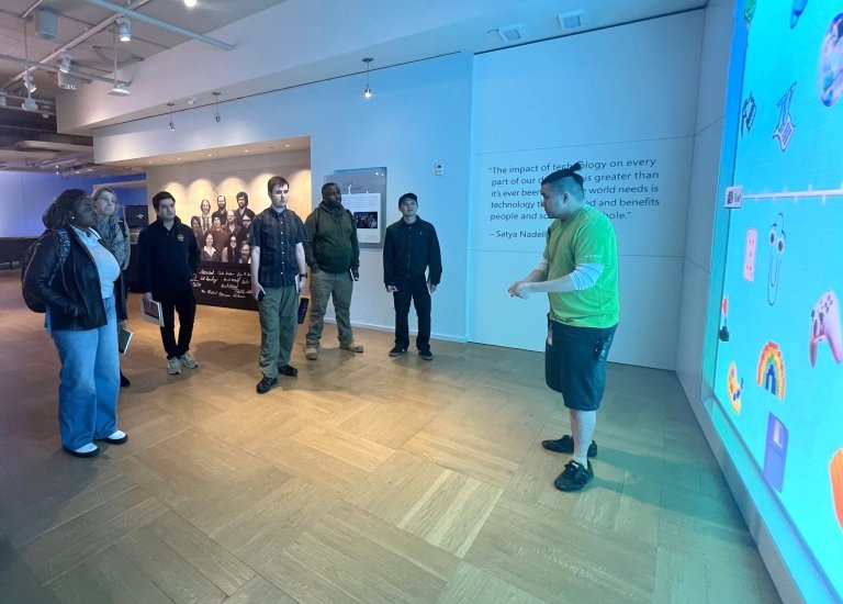 Students listen to a Microsoft tour guide, cast in a blue light