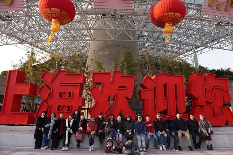 Students and staff in front of large statue of Chinese letters at foot of monument