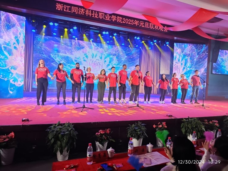 Students and staff in red shirts perform in a line on stage with lots of colored lights