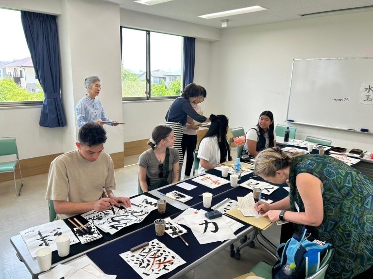 Students and teachers work on pages of Japanese calligraphy