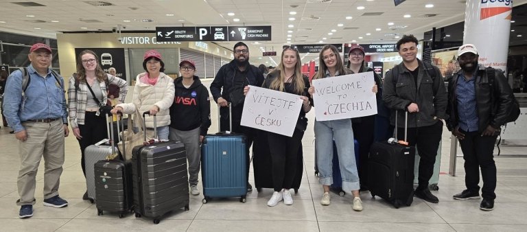 Students and faculty with luggage in airport holding signs written in foreign language