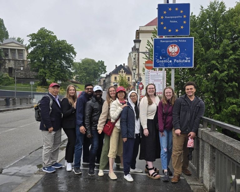 Students and faculty pose beneath sign on street in Poland