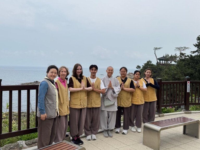 Students and faculty in uniform stand with a monk above a seascape
