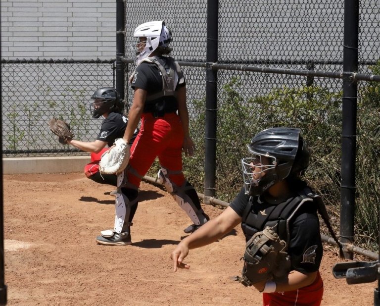 Softball players practice in uniform with mitts and helmets