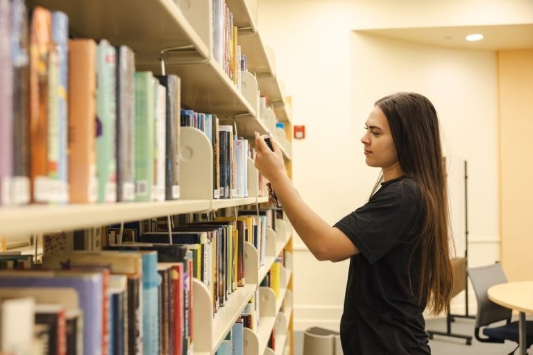 Student browsing books at library shelves