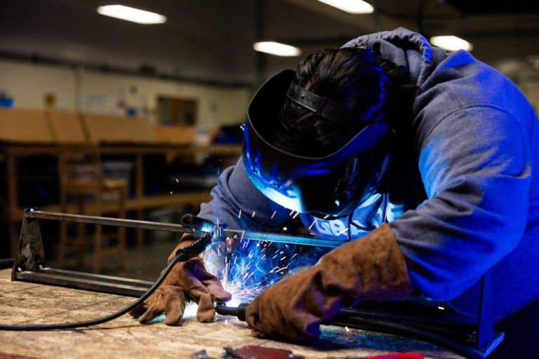 A student in protective gear welds a project