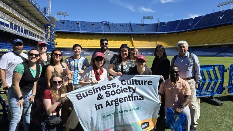 Students stand in stadium holding a banner that reads Business, Culture & Society in Argentina