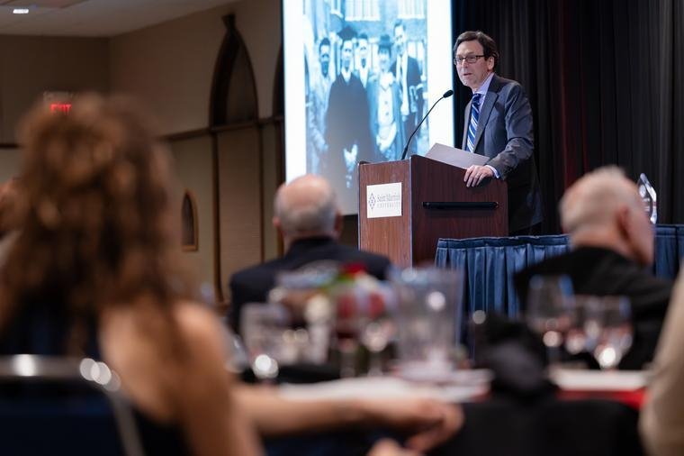 Governor Bob Ferguson speaks a podium with a picture of his uncle in the background