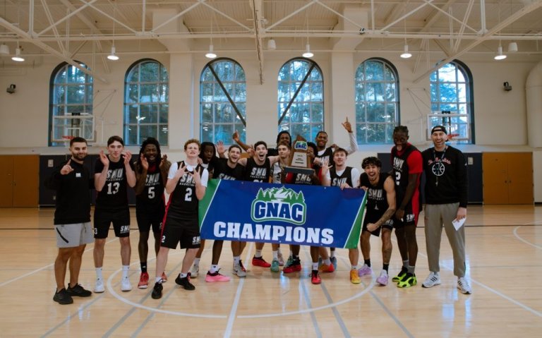 Men's basketball team and coaches hold GNA Champions banner on the basketball cout