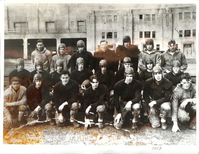 Football team photo in front of a brick building in black and white