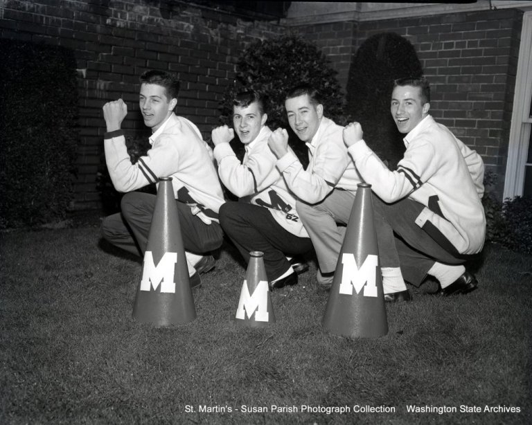Students crouch in a line with their fists raised in sync behind cones with "M" on them in black and white