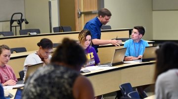 Dr. Aaron Coby assists students sitting in a lecture hall.