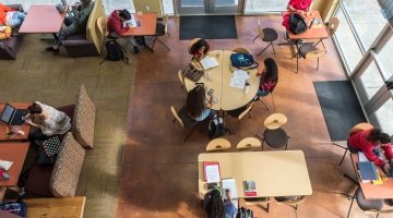 Overhead view of sitting area in Harned hall with lots of students grouped at various tables working alone or in company.