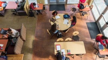 Overhead view of sitting area in Harned hall with lots of students grouped at various tables working alone or in company.