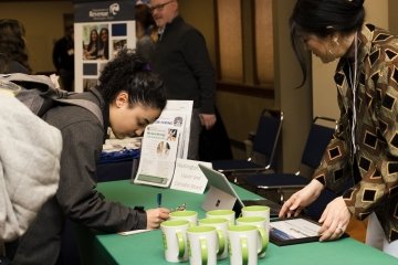 A student signs in at a table at a career fair, while the business representative works at a laptop.