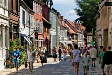 Many small groups of people walk down a street in the Netherlands, variegated shopfronts lining the entire street and curving away in the distance.