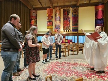 Fr. Peter reads in religious robes to a semicircle of students with bowed heads