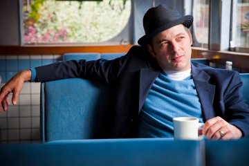 Jonathan Evison sits in a booth, looking out a window with a cup of coffee