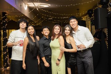 Students in semiformal dress pose underneath string lights