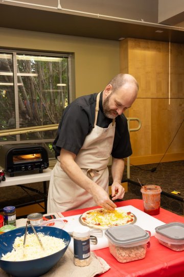 Fr. Peter making a pizza with ingredients spread around on a table